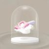 Stimulateur rose exposé sous une cloche transparente, reposant sur un nuage doux