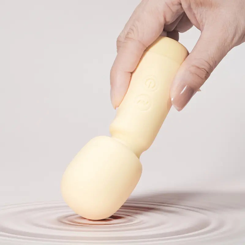 Main tenant le mini vibromasseur beige Ivy, posé sur une surface ondulée