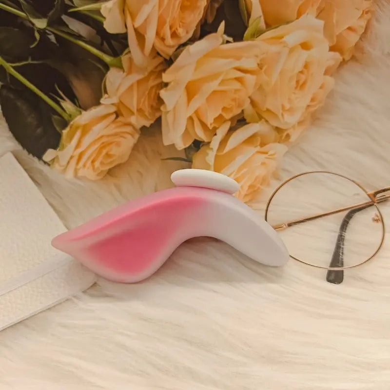Stimulateur intime Aisha posé sur un tapis doux, décoré de roses et d’accessoires féminins.